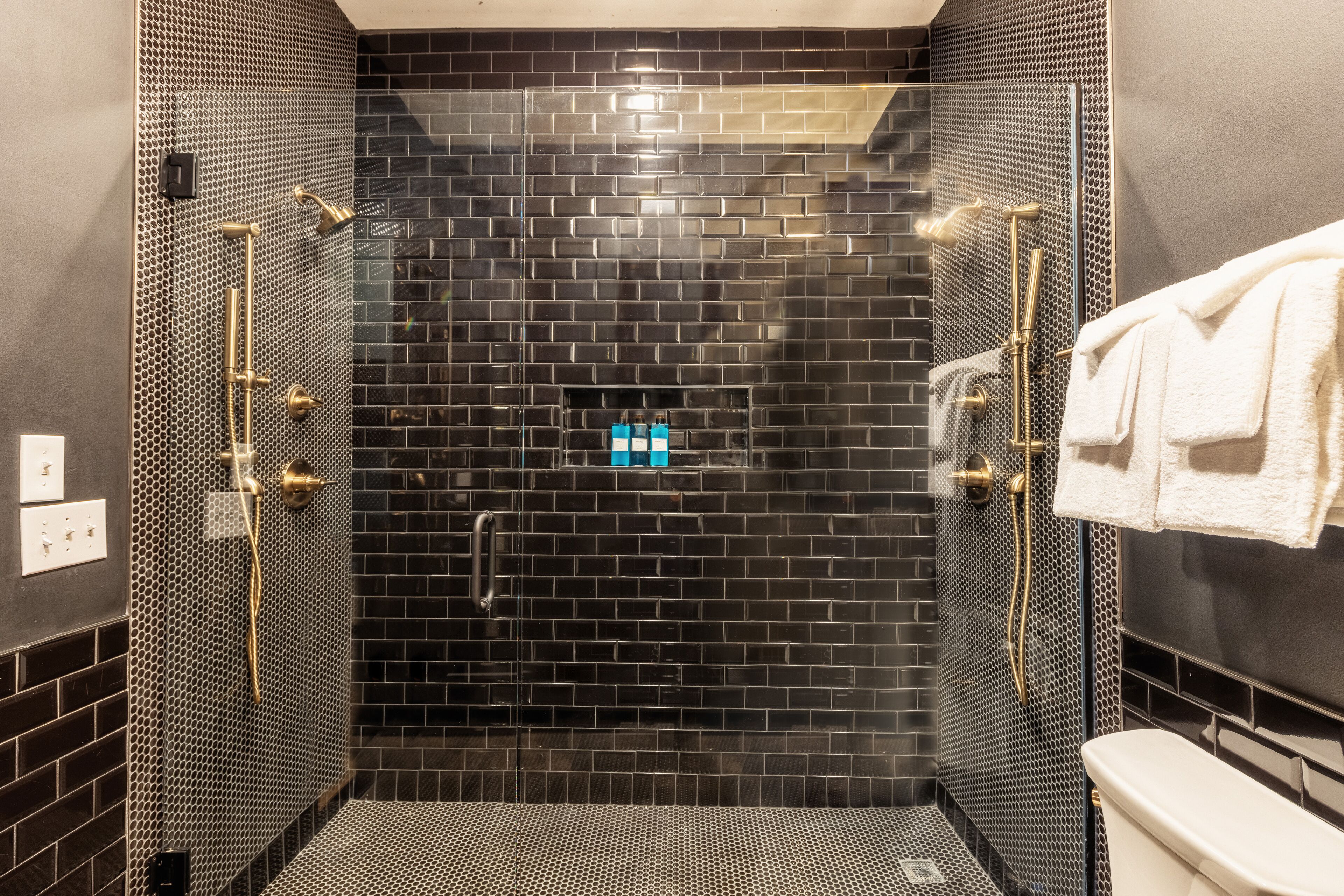 A modern bathroom with a black tiled shower area, a toilet, and a towel rack.