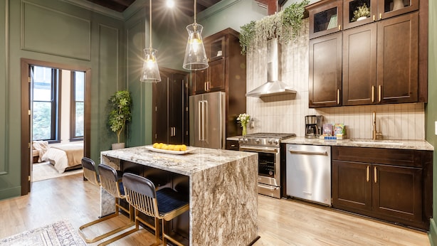 A modern kitchen with dark wood cabinets, stainless steel appliances, and a marble island. - Union Street Lofts (Nashville)