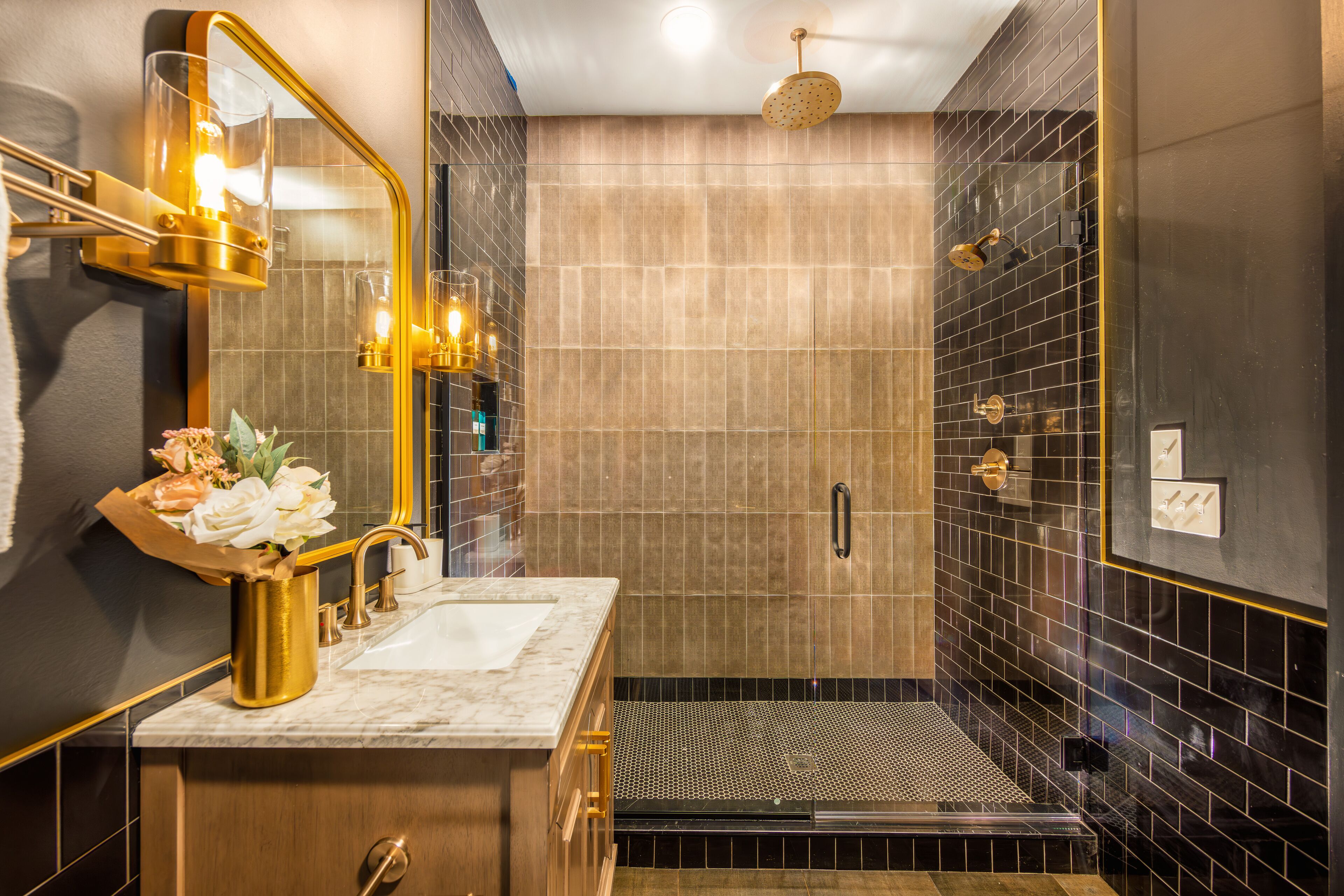 Une salle de bain moderne avec un lavabo en marbre, un miroir à cadre doré et un espace douche aux carreaux noirs.