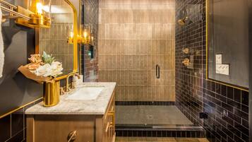 Une salle de bain moderne avec un lavabo en marbre, un miroir à cadre doré et un espace douche aux carreaux noirs.