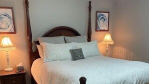 A neatly made bed with a wooden headboard, two bedside tables with lamps, and a bench at the foot of the bed. - Home Away From Home (St. Augustine)