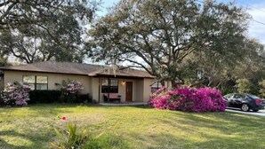 A single-story house with a front porch, a small garden, and a car parked in the driveway. - Home Away From Home (St. Augustine)
