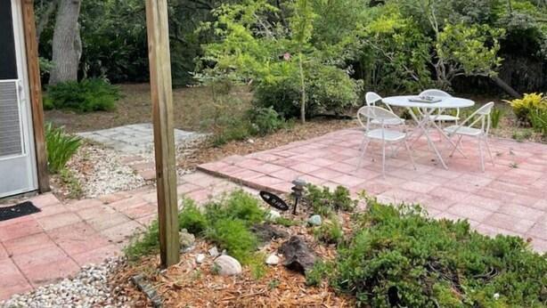 A patio with a pergola, outdoor seating, and a garden area with various plants and a small rock feature. - Home Away From Home (St. Augustine)