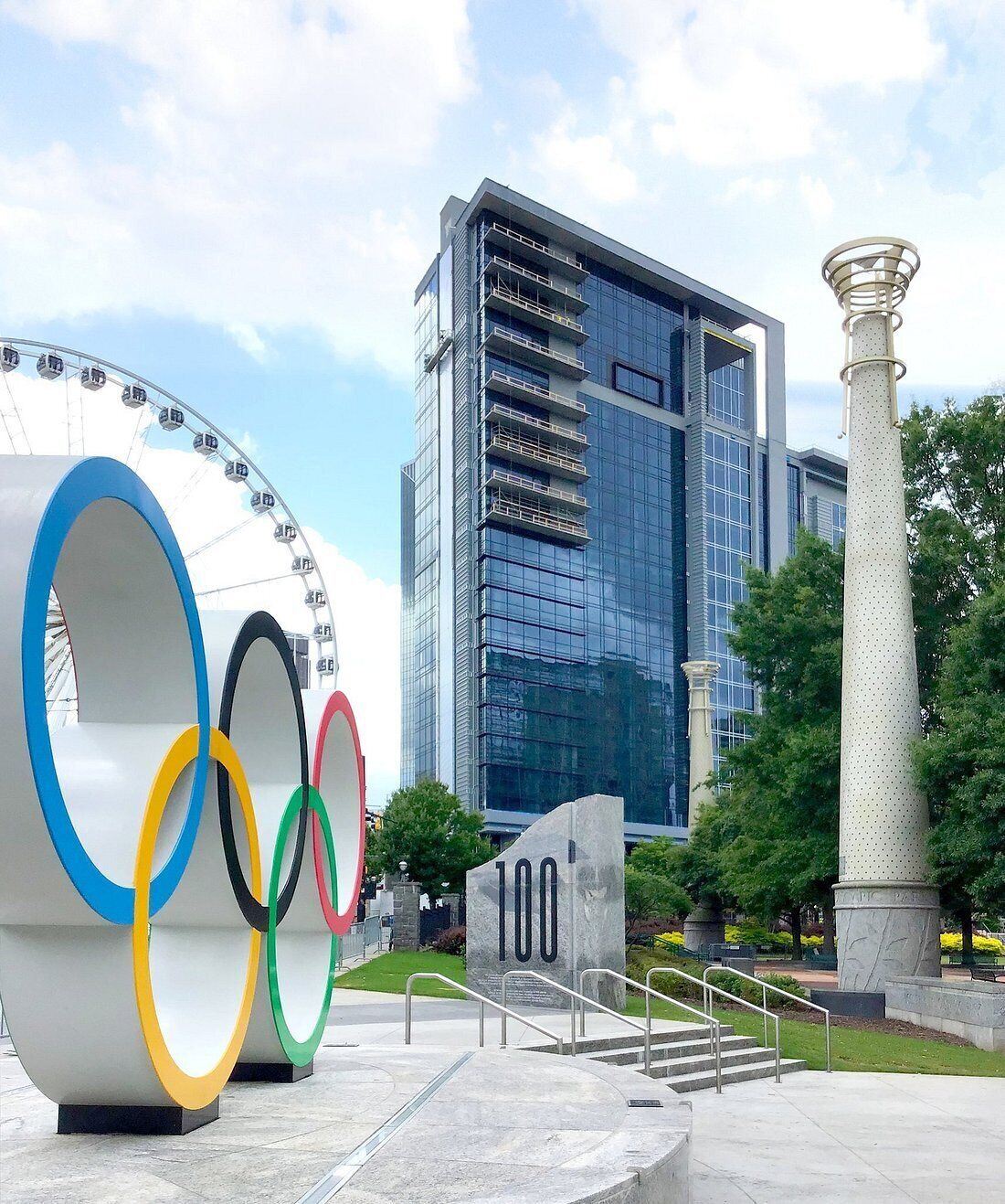 Un bâtiment moderne doté d’une façade en verre, d’une grande sculpture représentant les anneaux olympiques et d’une colonne sur laquelle est inscrit le chiffre 100.
