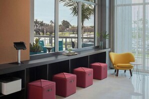Een moderne lobby met grote ramen, een gele stoel en rode poefs.