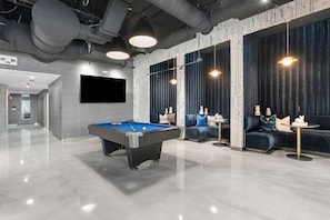 Une table de billard moderne, conçue pour l’intérieur, avec un jeu de billard, un canapé et un téléviseur fixé au mur.