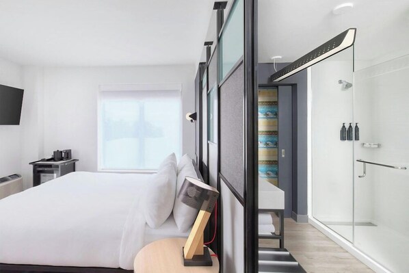 Een moderne hotelkamer met een bed, een bureau, een douche en een groot raam.