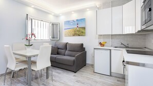 A modern kitchen with white cabinets, a grey sofa, a dining table with chairs, and a small refrigerator. - Home2Book Chill & Sun Colina Blanca & Pool, Adeje (Adeje)