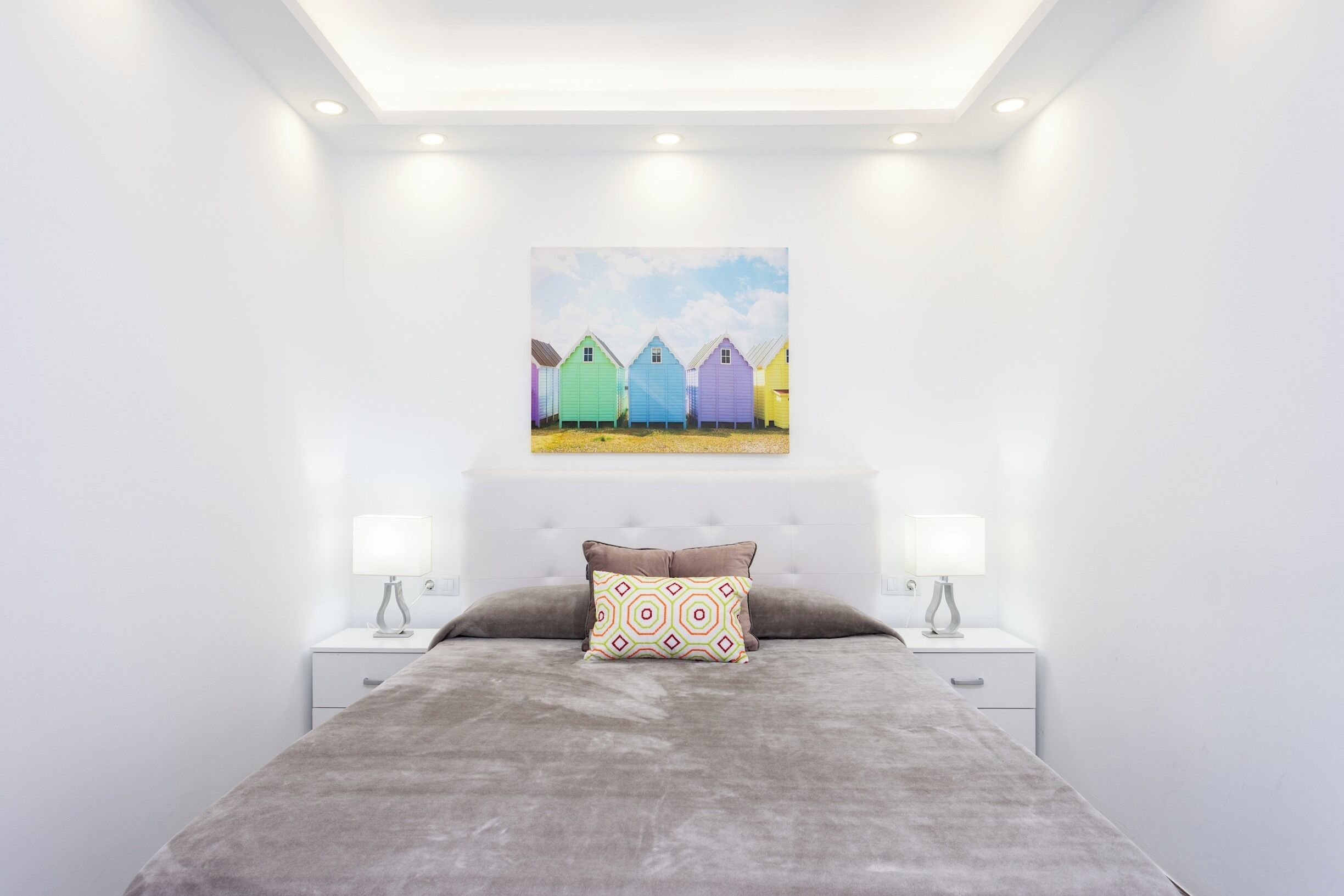 Una camera da letto con un letto, due comodini, una testiera e un quadro raffigurante case colorate.