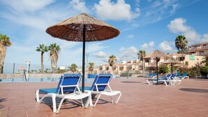 A poolside area with lounge chairs and umbrellas, a clear sky, and palm trees. - Home2Book Chill & Sun Colina Blanca & Pool, Adeje (Adeje)