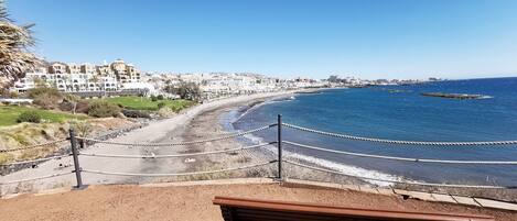 A coastal view with a sandy beach, a wooden bench, and a rope barrier.