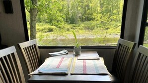 Pöydällä on kasvi ja papereita, ja pöytä on sijoitettu ikkunan eteen, josta avautuu näkymä metsään.
