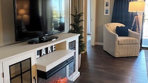 Una sala de estar con chimenea, televisor, un sillón a rayas y un cartel que dice "WELCOME TO THE LAKE".