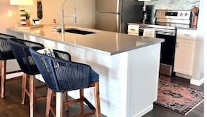 Una cocina moderna con una isla central, taburetes de bar, electrodom ésticos de acero inoxidable y una alfombra estampada.