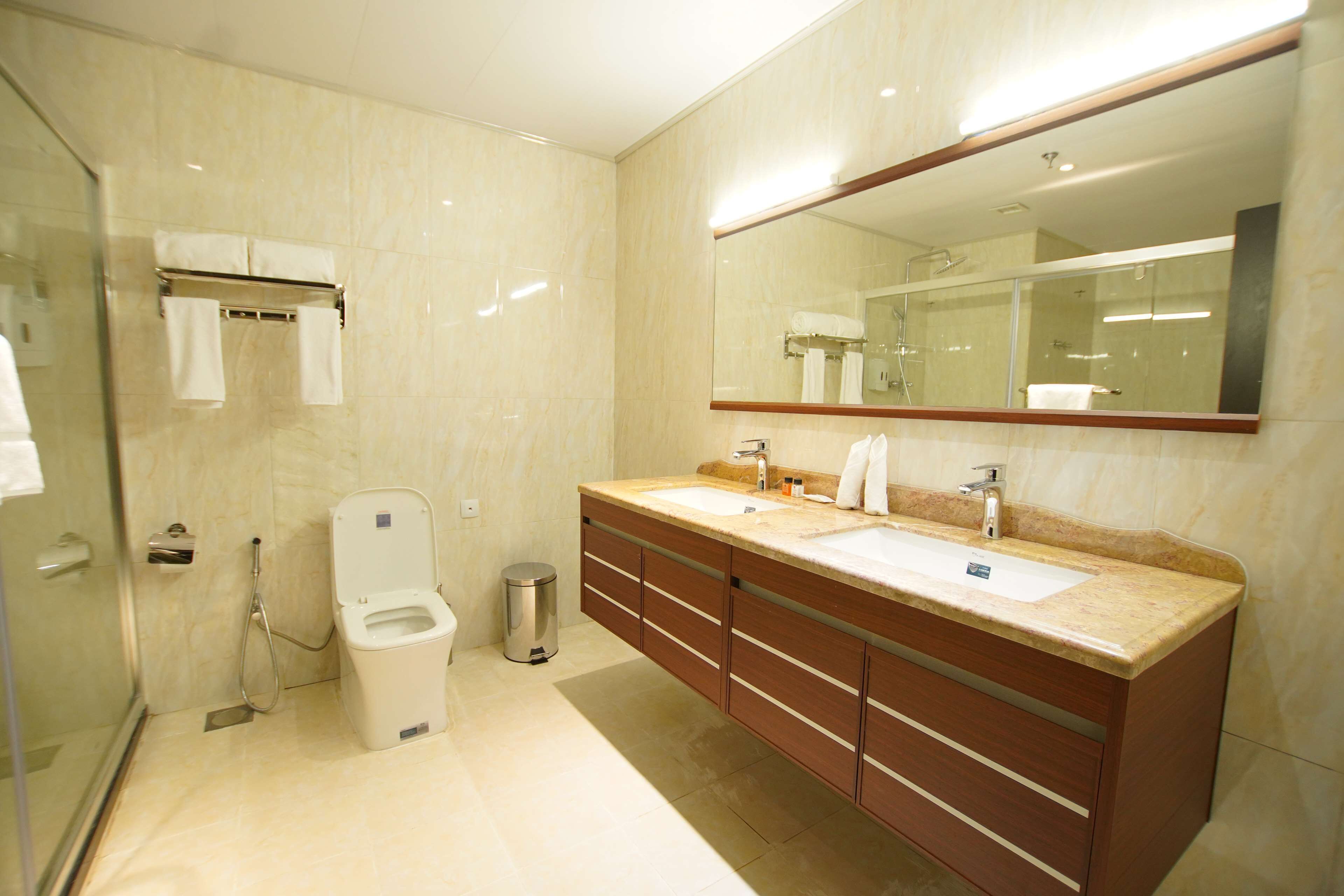 Un bany modern amb dutxa de vidre, un vàter i un lavabo doble amb un mirall gran.