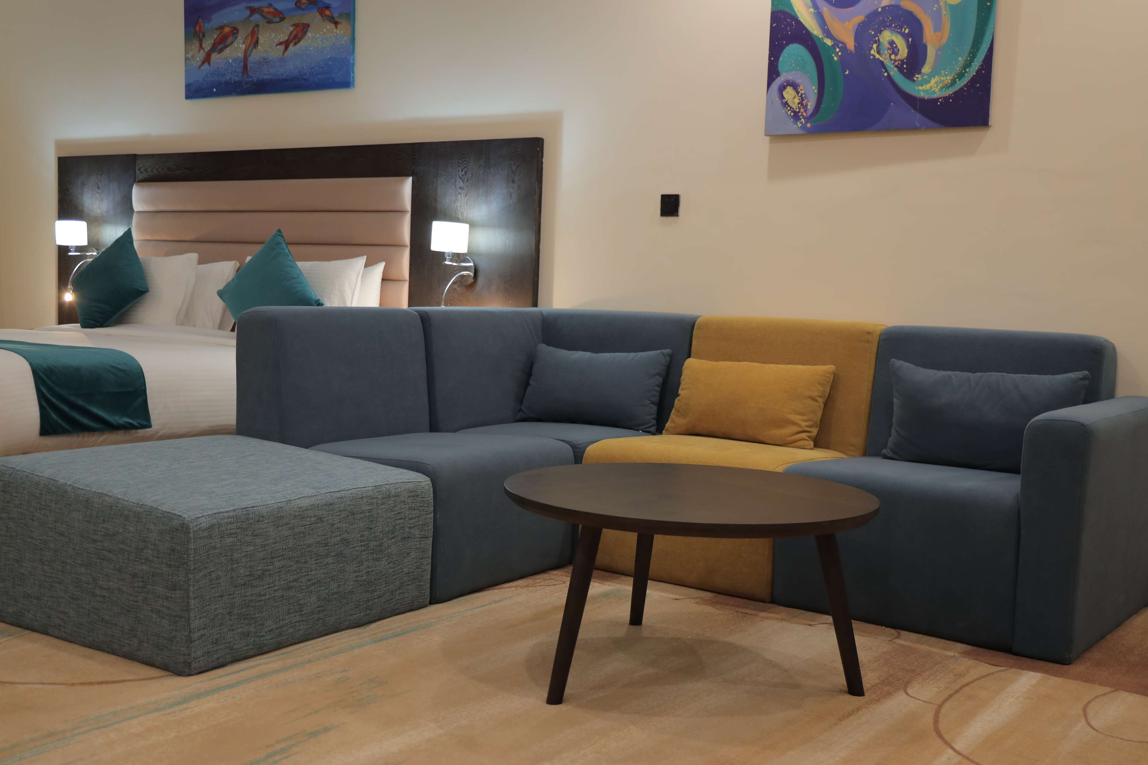 A modern hotel room with a large bed, a sofa, a coffee table, and artwork on the walls.