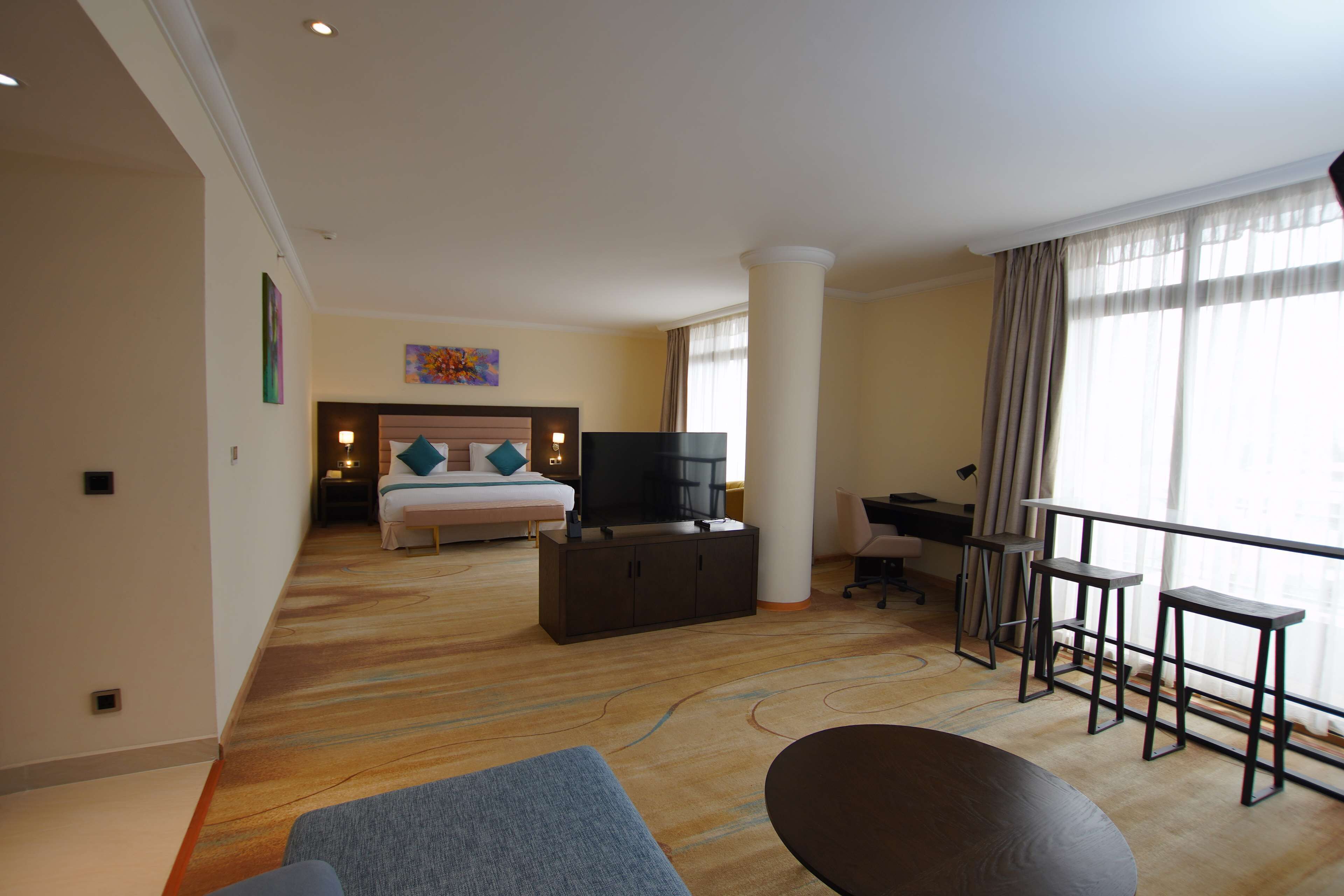 Habitación de hotel con cama, televisión, escritorio y balcón con barandilla.