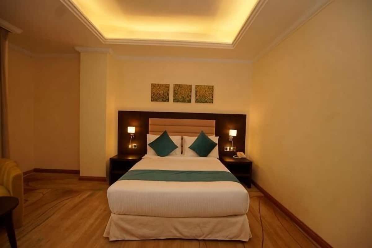 A hotel room with a bed, two bedside tables, a nightstand, a chair, and a ceiling light.
