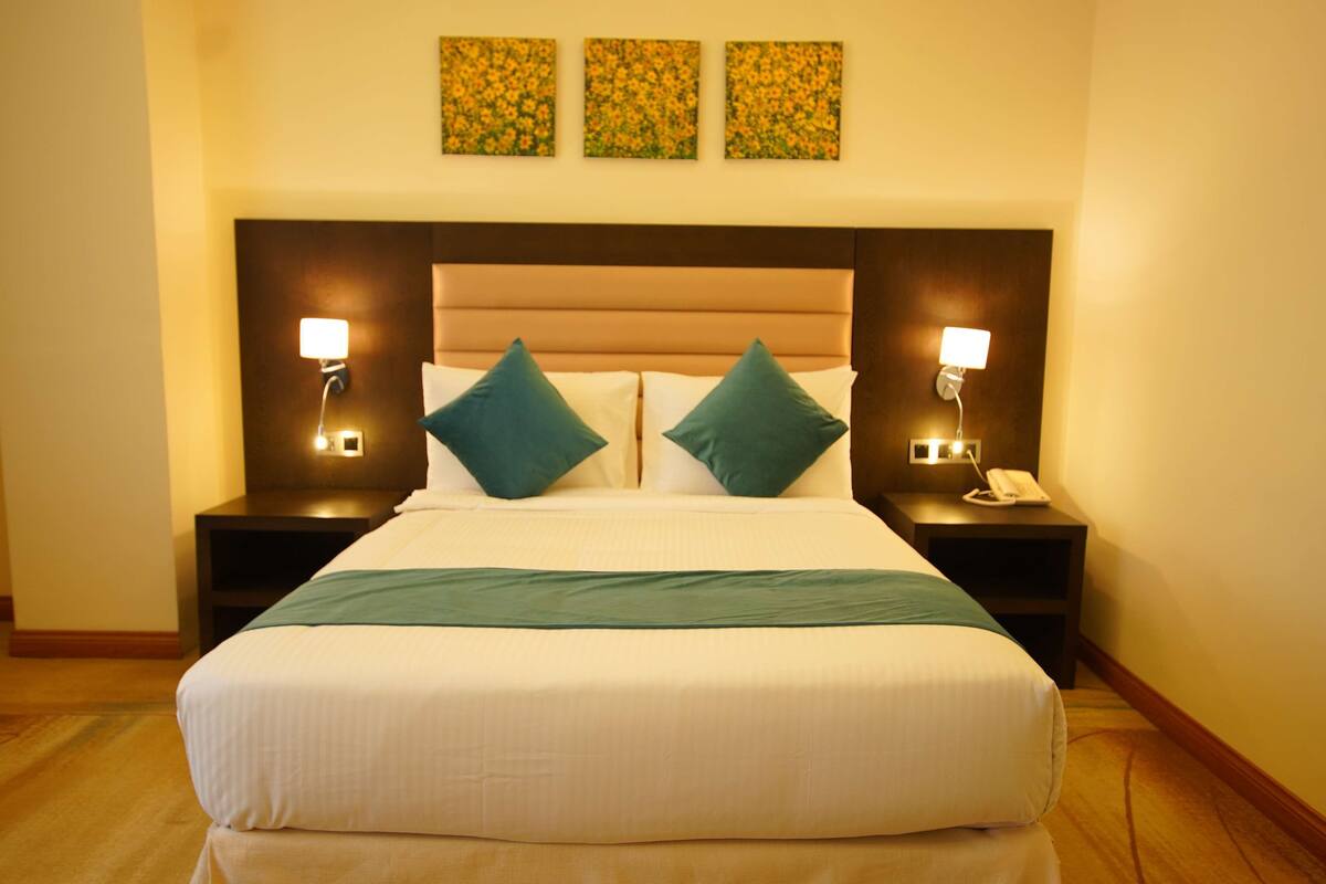 A hotel room with a large bed, two nightstands, a telephone, and three wall-mounted lamps.