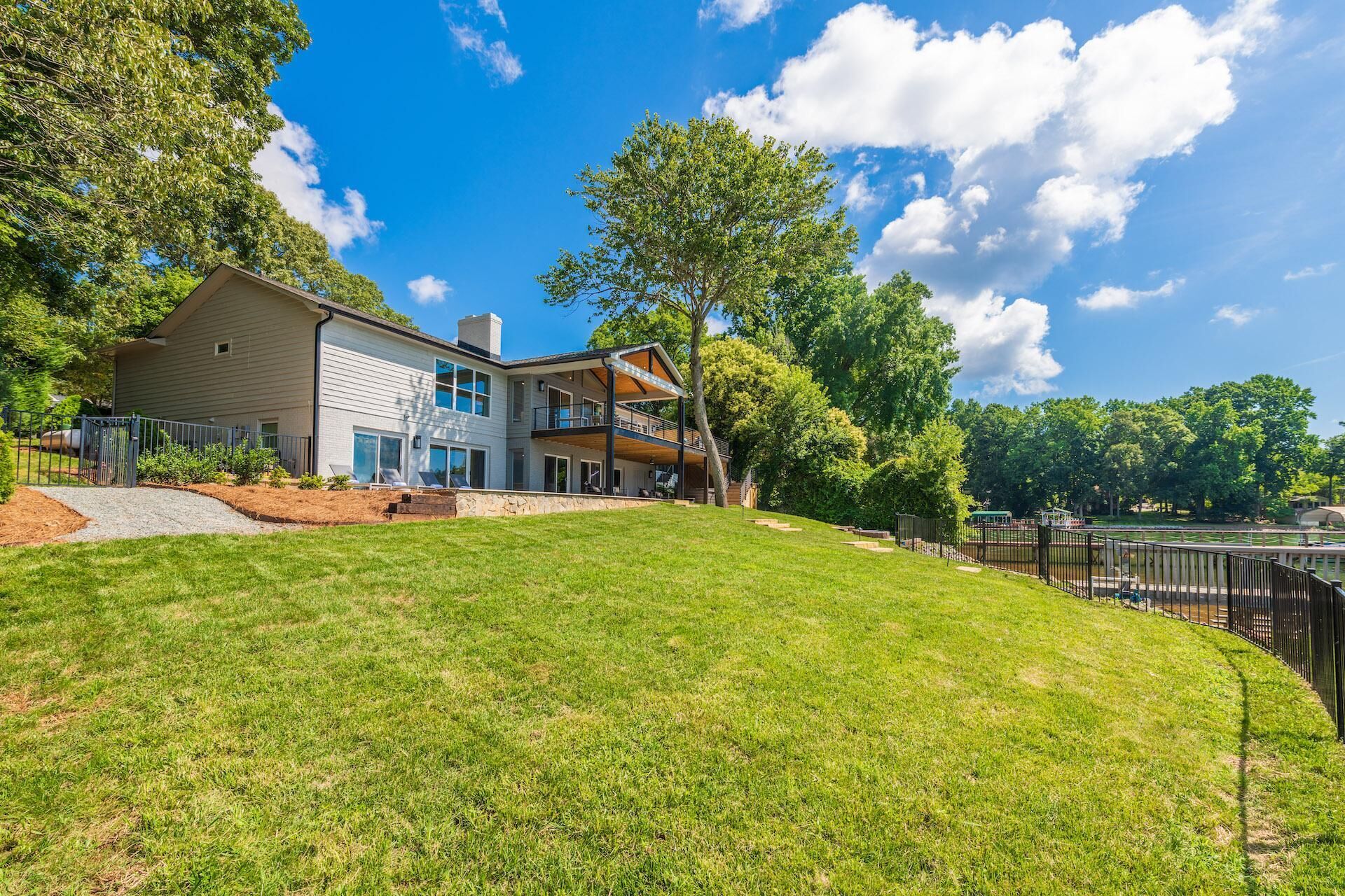 A modern two-story house with a large front lawn, a covered patio, and a view of a lake.