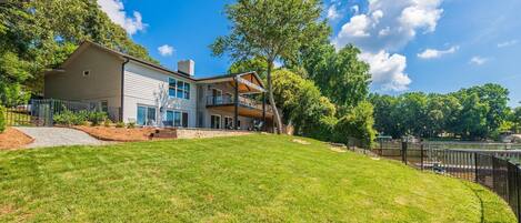 A modern two-story house with a large front lawn, a covered patio, and a view of a lake.