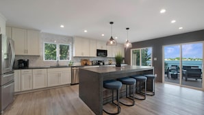 A modern kitchen with a large island, bar stools, and a view of the outdoors. - Lakeshore Adrift (Denver)