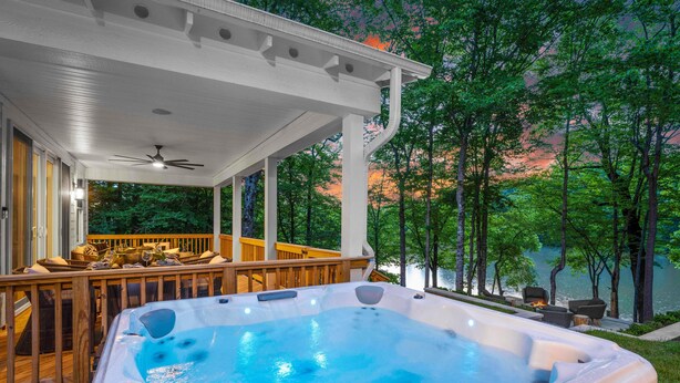 Un jacuzzi bajo una terraza cubierta con vistas a un lago y árboles.