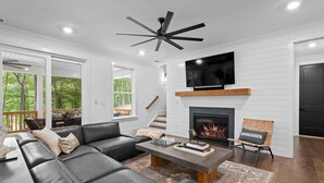 Una sala de estar moderna con un sofá seccional de cuero negro, una mesa de centro de madera, una chimenea y un televisor montado.