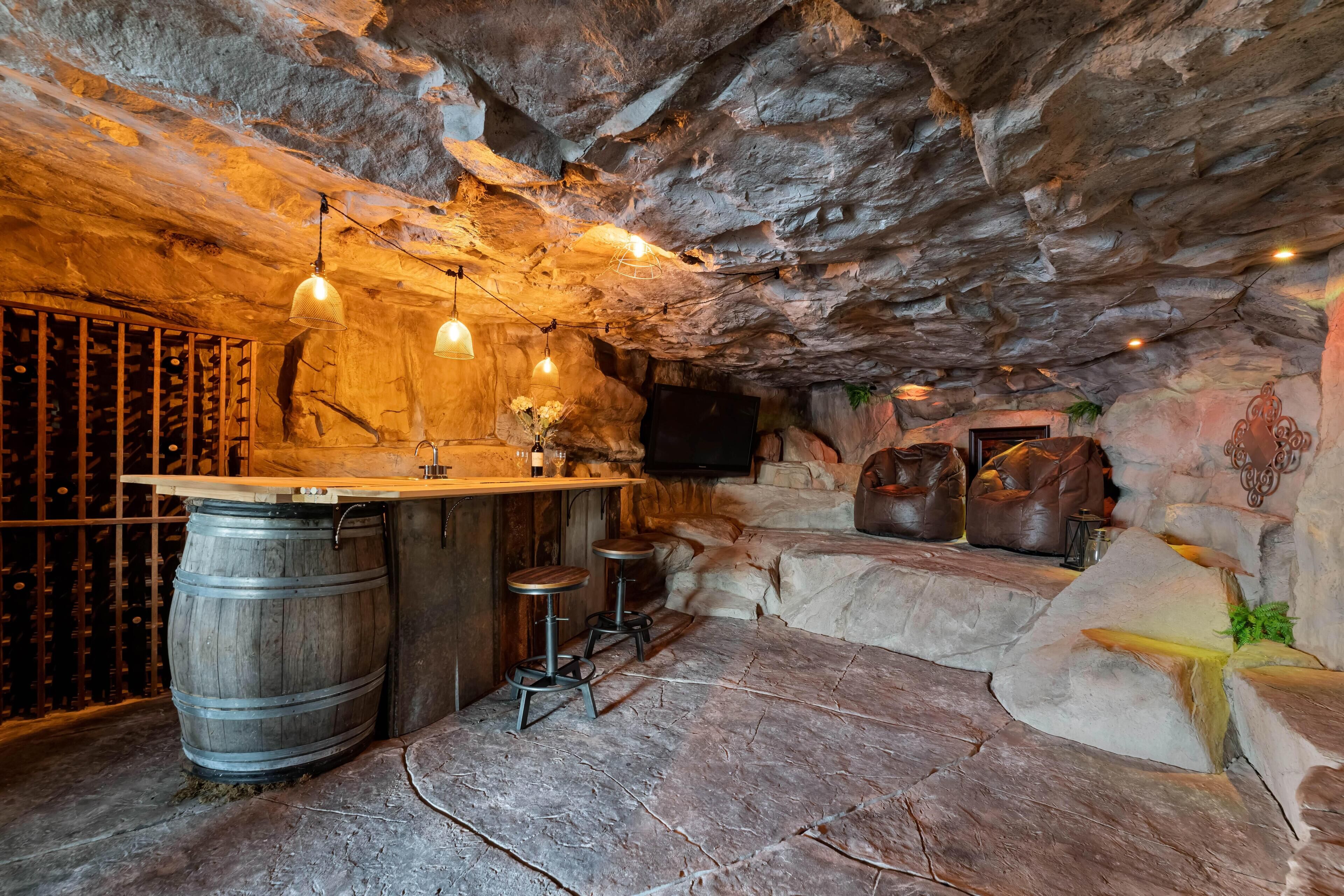 Un rústico área de bar con barra de madera, paredes de piedra y luces colgantes.