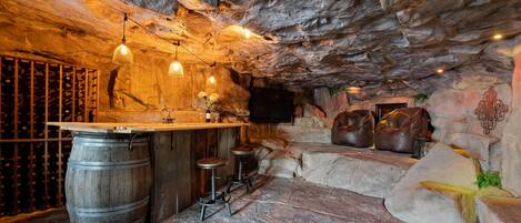 Un rústico área de bar con barra de madera, paredes de piedra y luces colgantes.