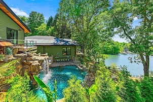 Una casa con piscina rodeada de abundante vegetación y vista al lago.