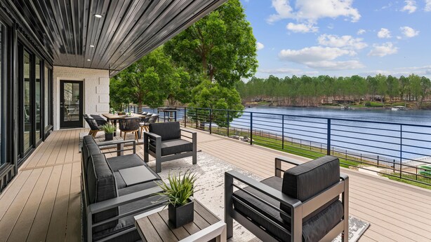 A covered outdoor deck with seating, a view of a lake, and a forested area in the background. - Salience Path W/heated Pool & Game Room (Mooresville)
