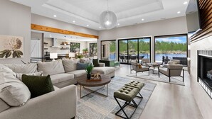 A modern living room with a sofa, coffee table, and ottoman, a dining area with chairs, and a kitchen in the background. - Salience Path W/heated Pool & Game Room (Mooresville)
