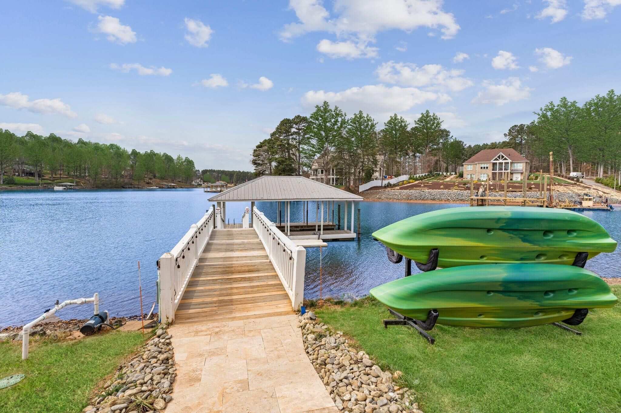 Un muelle de madera que lleva a una casa junto al lago, con kayaks en el césped.