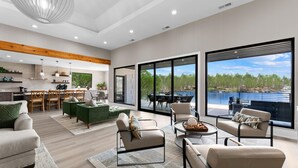 A spacious living area with modern furniture, a dining set, and large windows offering a view of a lake. - Salience Path W/heated Pool & Game Room (Mooresville)