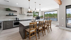 A modern kitchen with a large island, wooden chairs, pendant lighting, and a view through large windows. - Salience Path W/heated Pool & Game Room (Mooresville)