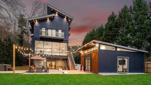 A modern two-story house with a garage, outdoor seating area, and string lights.