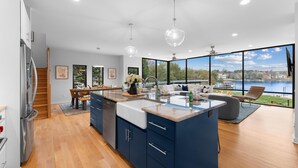 A modern kitchen with a large island, wooden flooring, and a view of a lake.