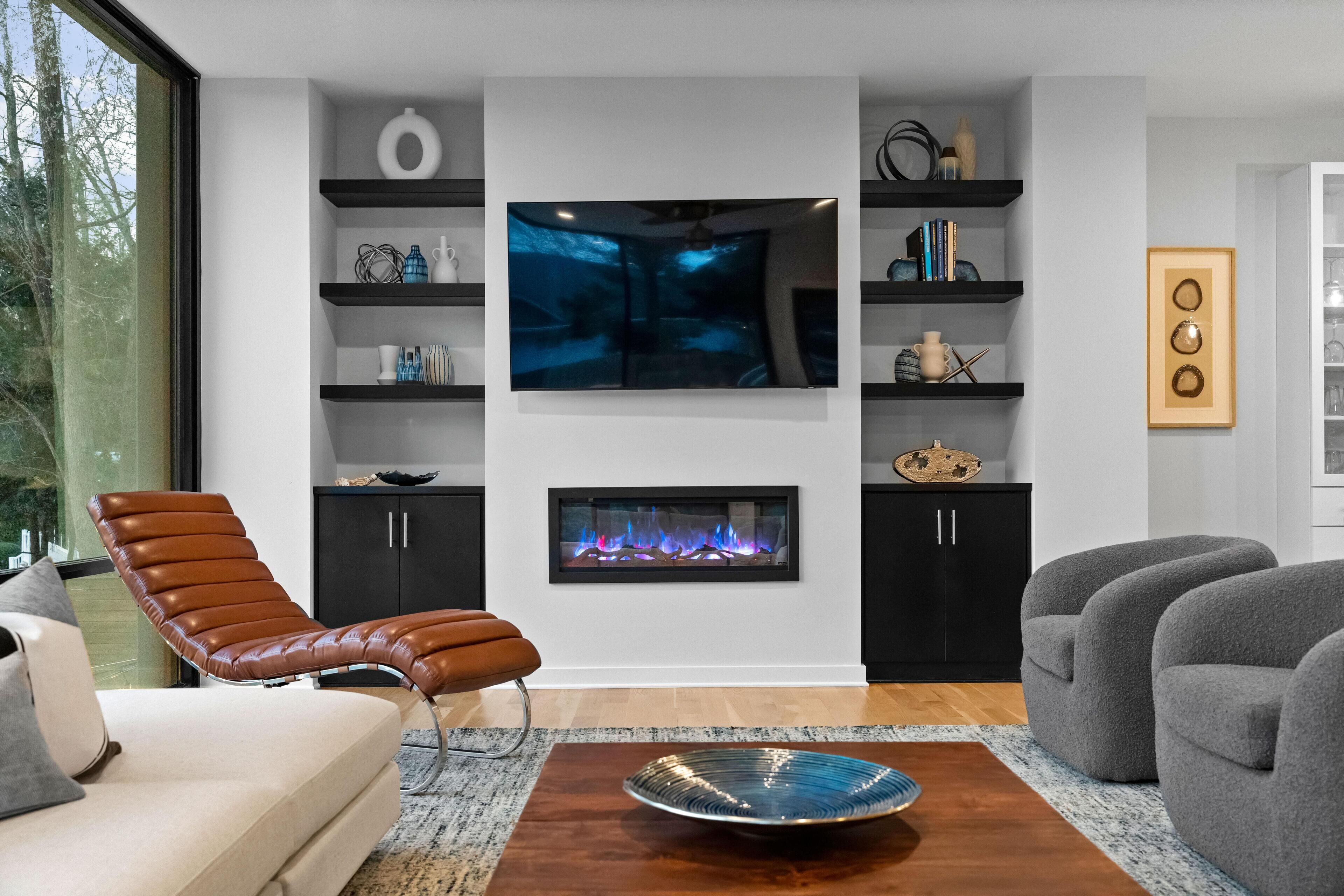 Un salon moderne doté d’une cheminée, d’un téléviseur fixé au mur et d’un coin salon confortable.