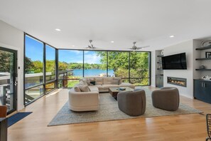 A modern living room with a large window, a fireplace, and a TV. - Blue Haven W/game Room, Hot Tub & Optional Boat Rental (Mooresville)