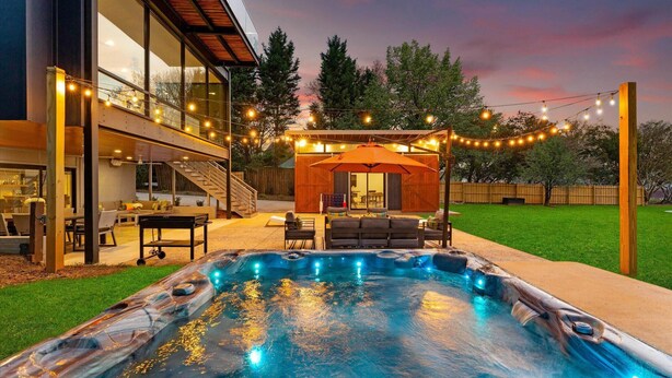 A modern house with a hot tub, outdoor seating, and string lights.