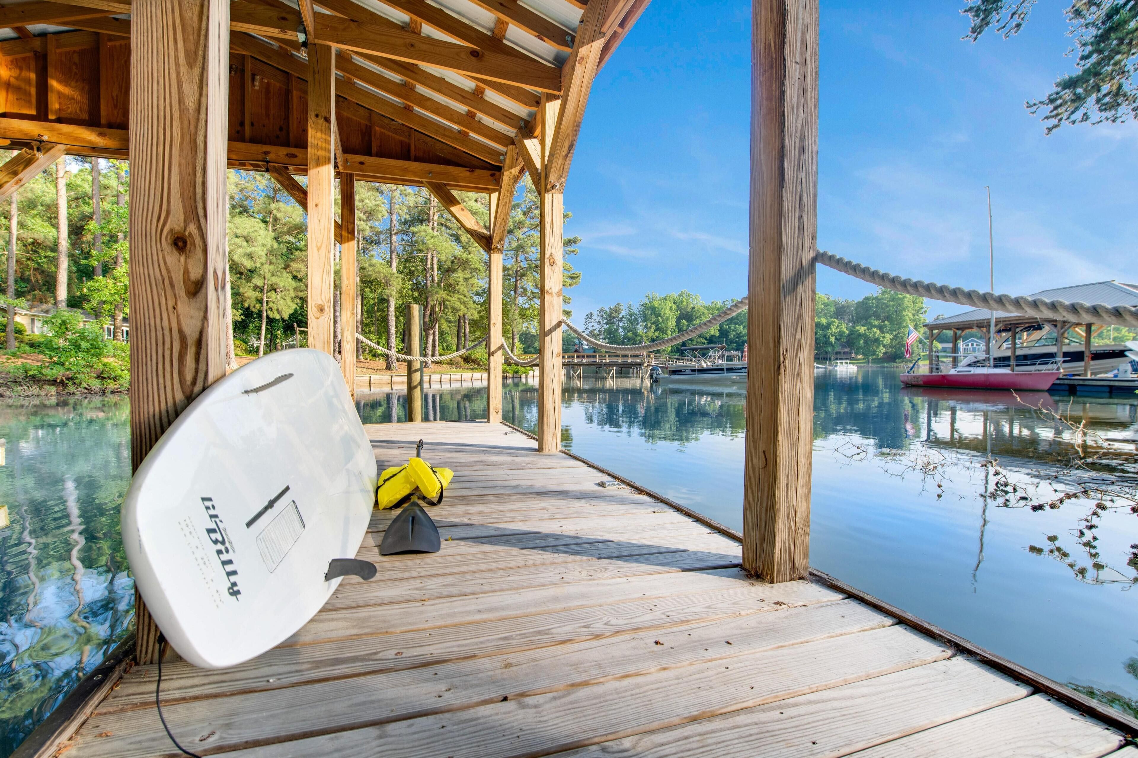 A wooden dock extending over a calm lake with a clear view of boats and a covered area.
