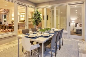 A modern dining area with a long table set for six, surrounded by glass doors leading to a kitchen and a bedroom. - Barefoot on Blarney (Mooresville)