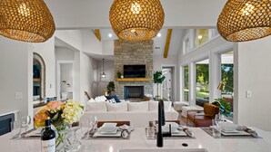 A modern living room with a stone fireplace, white sofas, and a dining area with a white table set for six. - Hogan Crest (Mooresville)