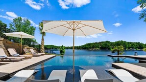 A poolside area with lounge chairs and umbrellas, a clear view of a lake, and a stone staircase leading down to the water. - Hogan Crest (Mooresville)