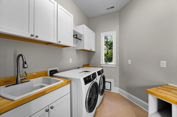 A laundry room with a washing machine, a sink, and cabinets.
