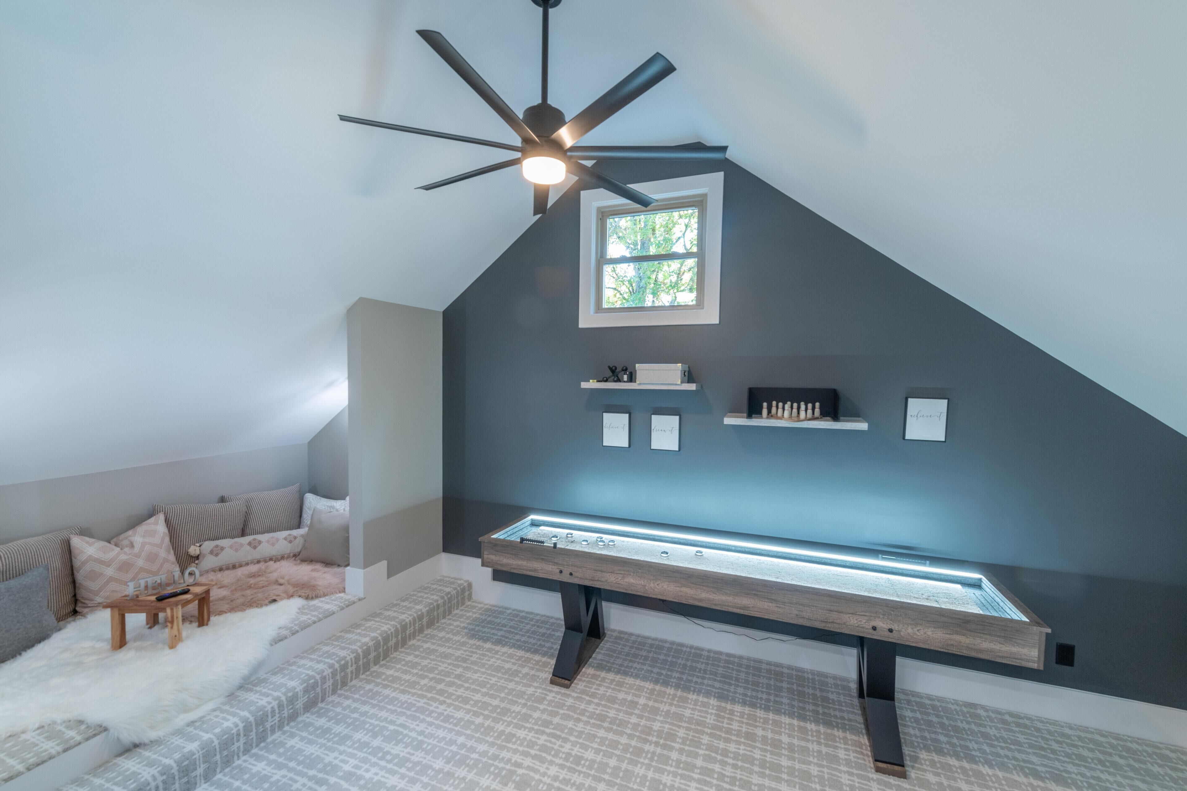 Ein modernes Schlafzimmer im Dachgeschoss mit schrägen Wänden, Deckenventilator, Dachfenster, eingebautem Sitzplatz und einer kleinen Regaleinheit.