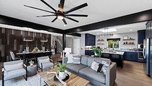 A modern open-plan living and dining area with a kitchen, featuring a ceiling fan, dark wood paneling, and a mix of seating options. - Channel Marker (Mooresville)