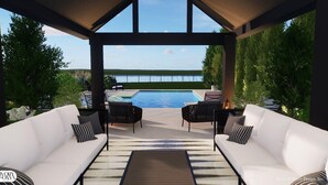 A covered outdoor seating area with two white sofas and a wooden table, overlooking a swimming pool and a view of the water. - Channel Marker (Mooresville)