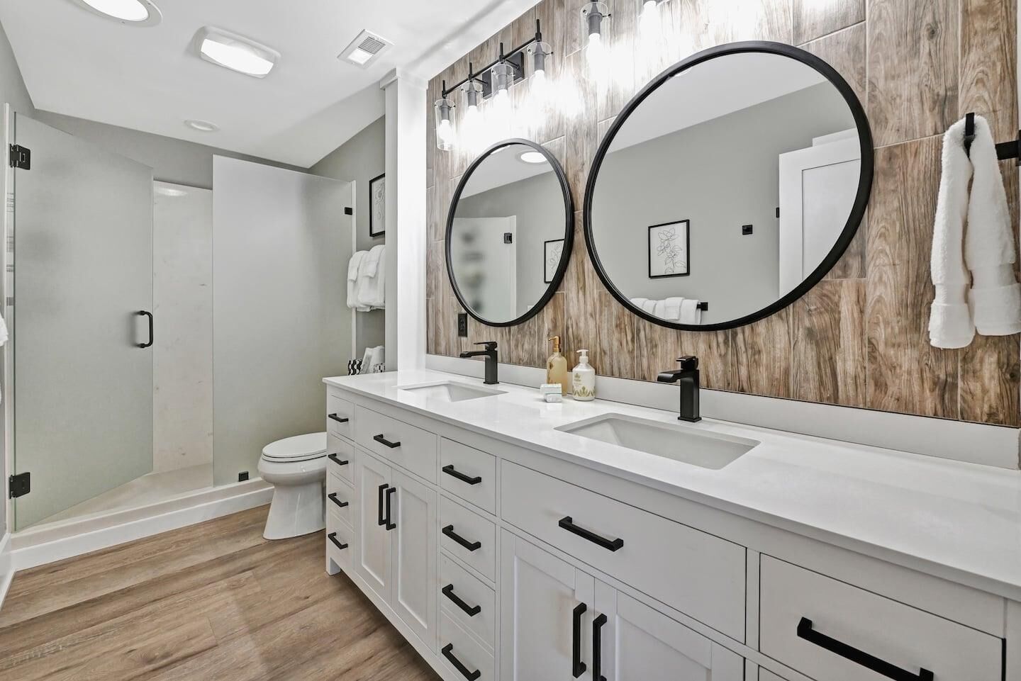 A modern bathroom with two sinks, a large mirror, and a shower area.
